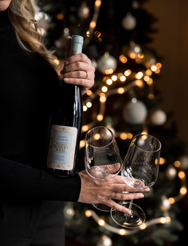 Robert Weil Kiedrich Gräfenberg Riesling Spätlese bottle held with wine glasses in front of a decorated Christmas tree