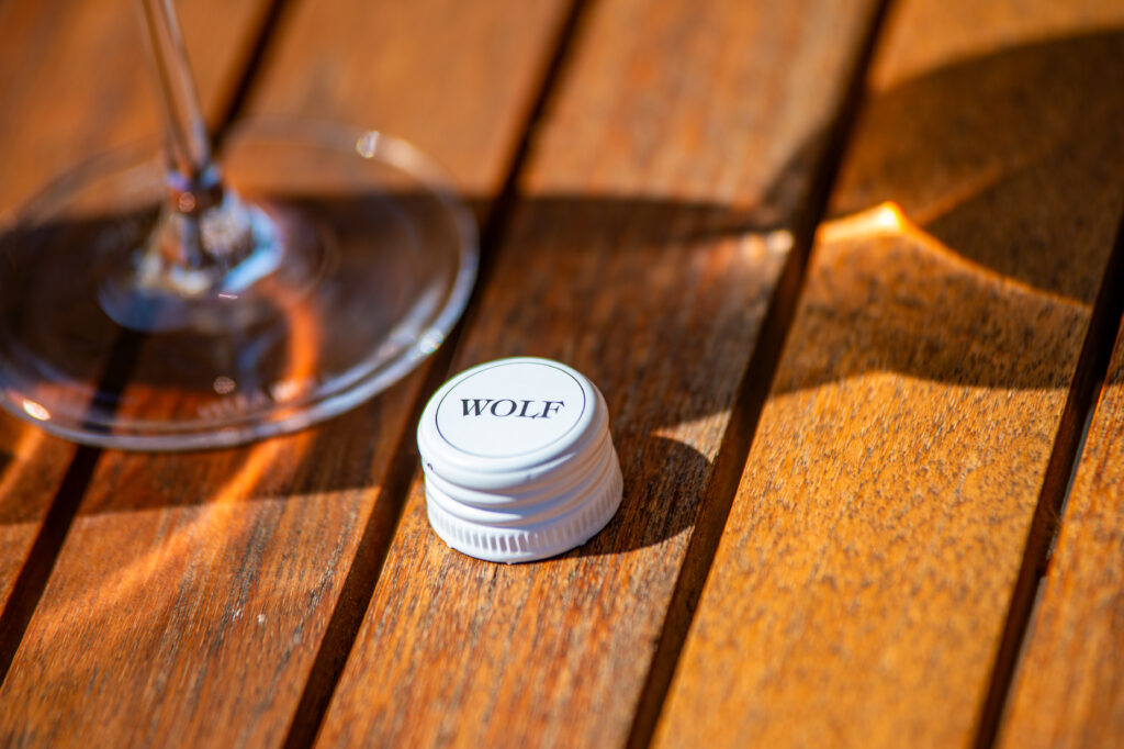 Villa Wolf Cap sits on a table with a wine glass. Sun shines rays through the glass on to the table.