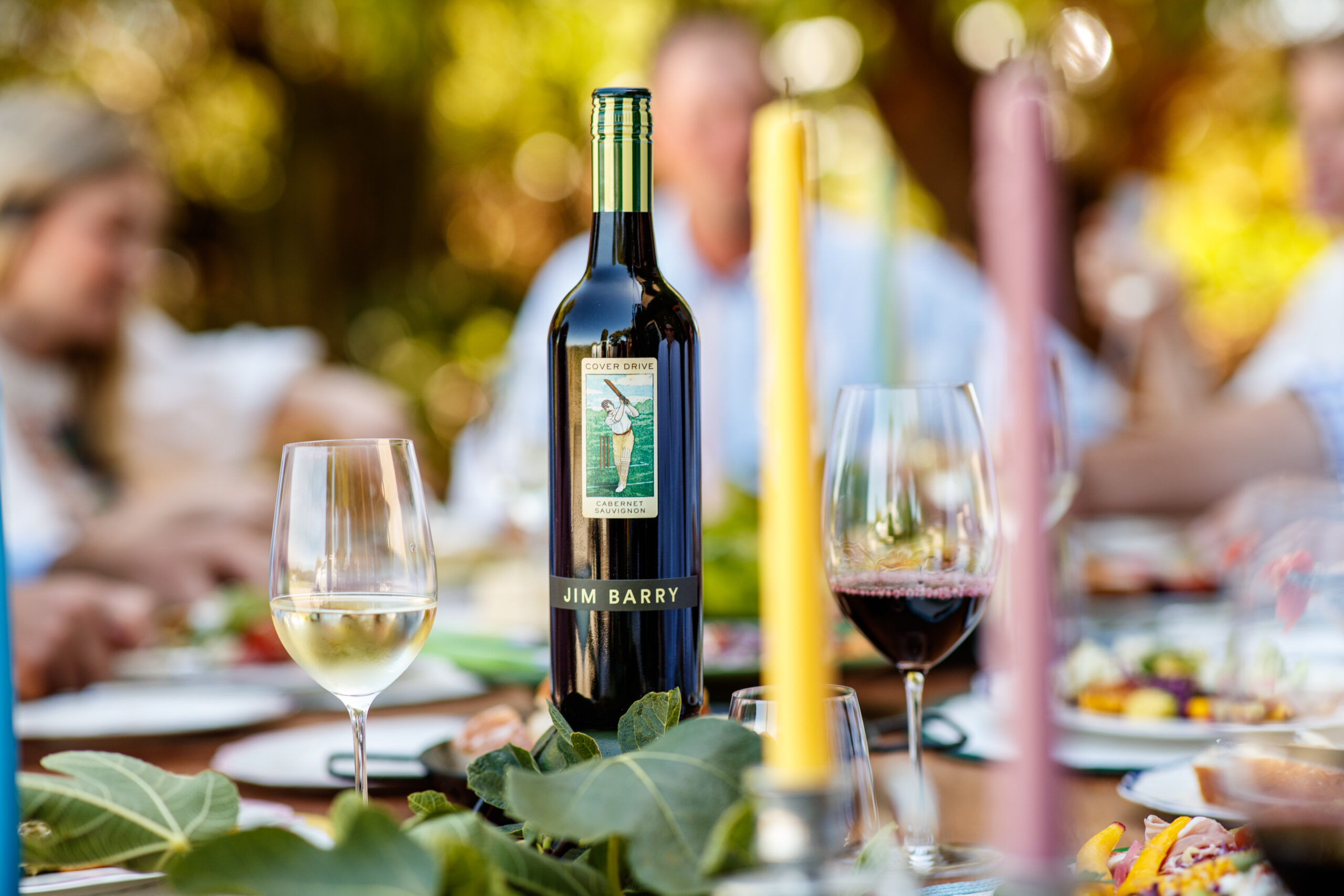 Jim Barry The Cover Drive Cabernet Sauvignon bottle sits on the dinner table surrounded by full glasses and candles.
